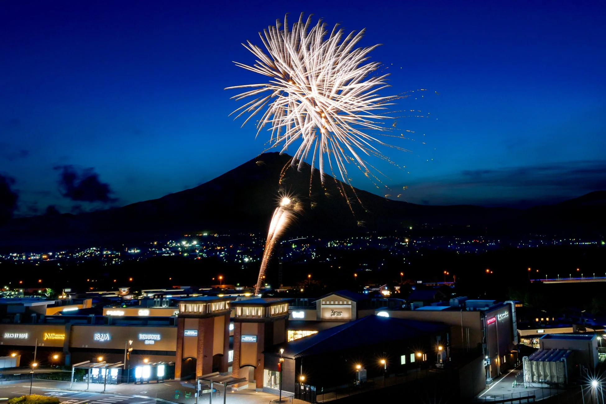富士山を背景に打ち上がる花火とライトアップされたアウトレットの夜景