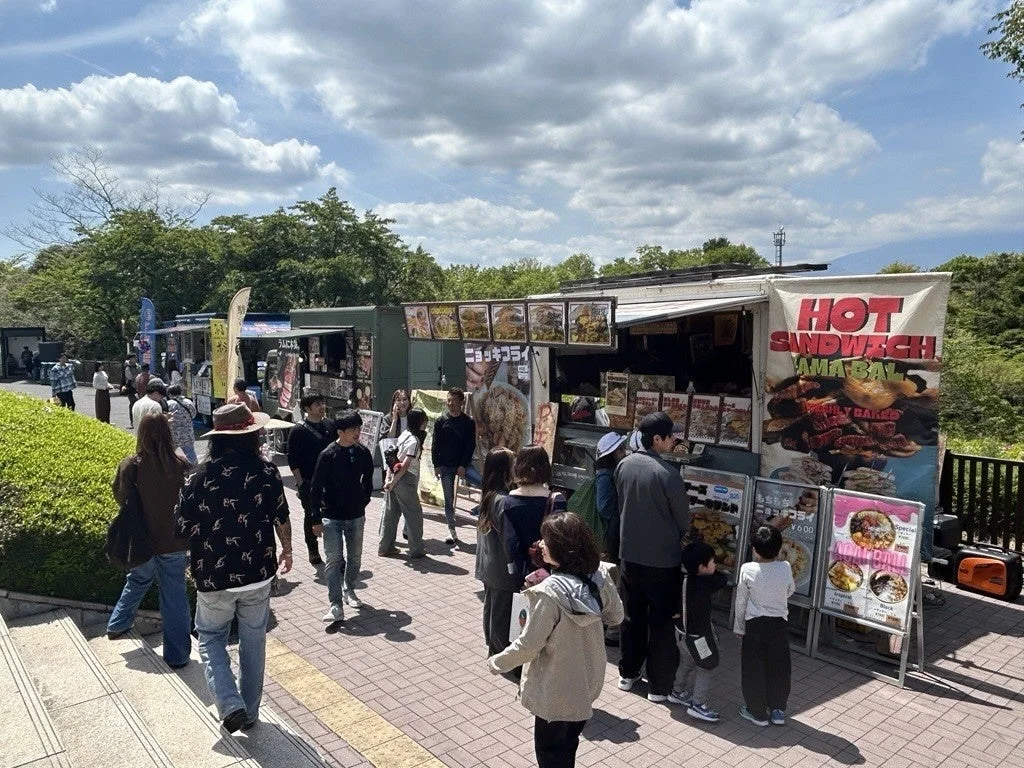 屋外イベントで多くの人々がフードトラックや屋台に集まっている様子