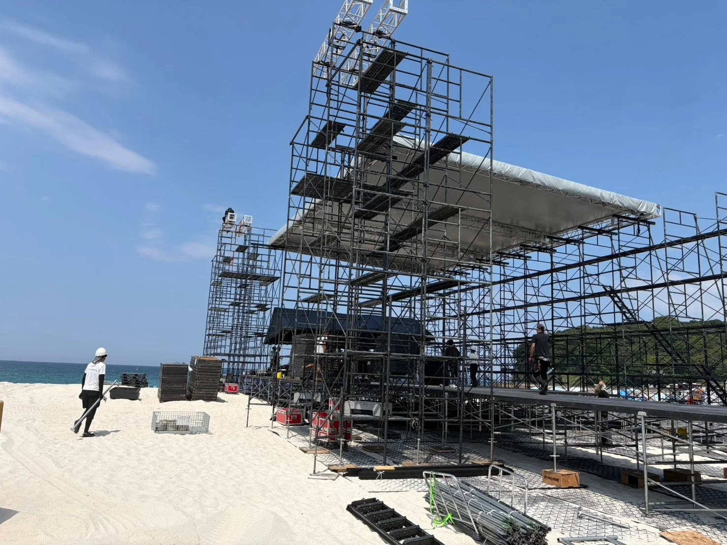 白い砂浜に巨大な足場が組まれ、屋外イベント用のステージが建設中の様子