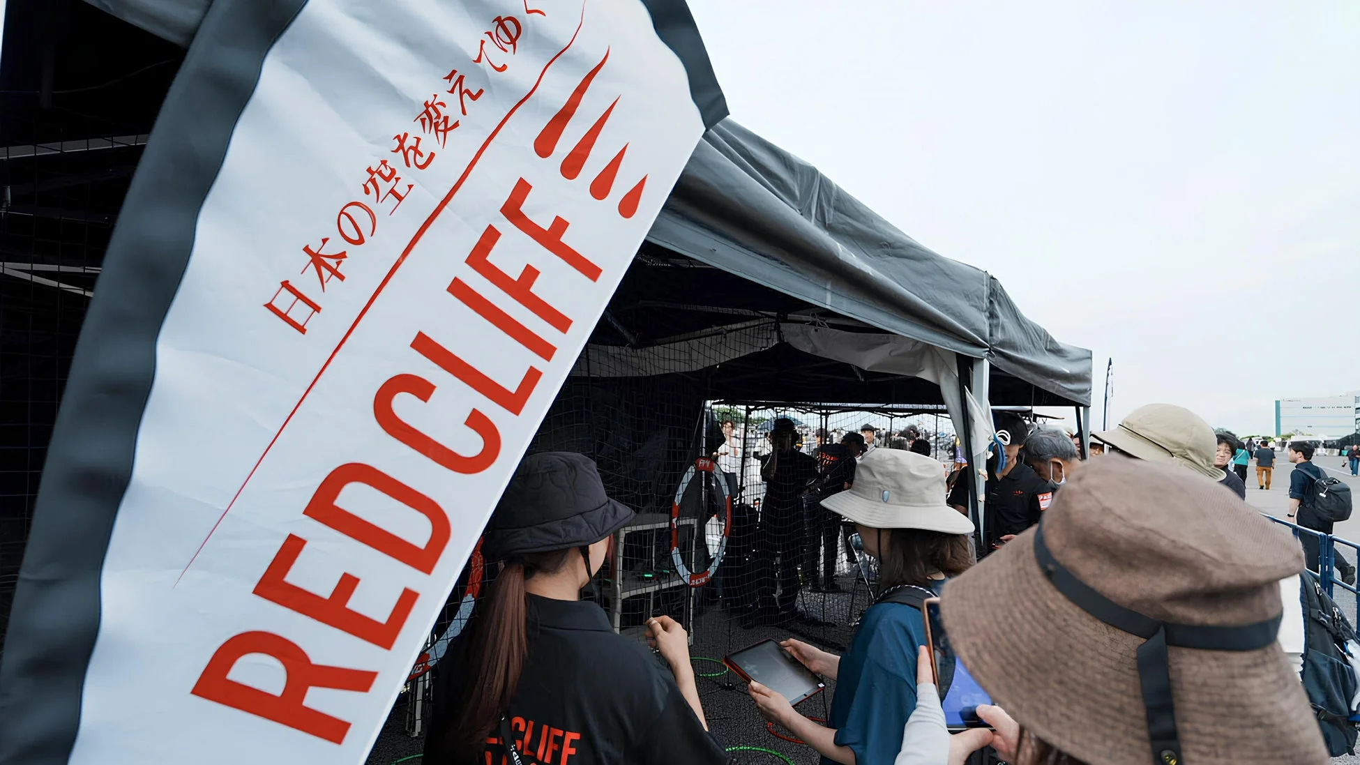 屋外イベント会場で、多くの人々がテントの周りに集まっている様子