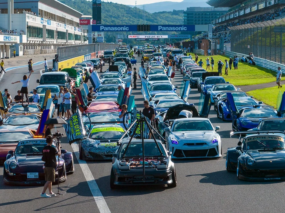 富士スピードウェイのサーキットで、改造車やスポーツカーが多数集まりパレードランのために整列している様子。