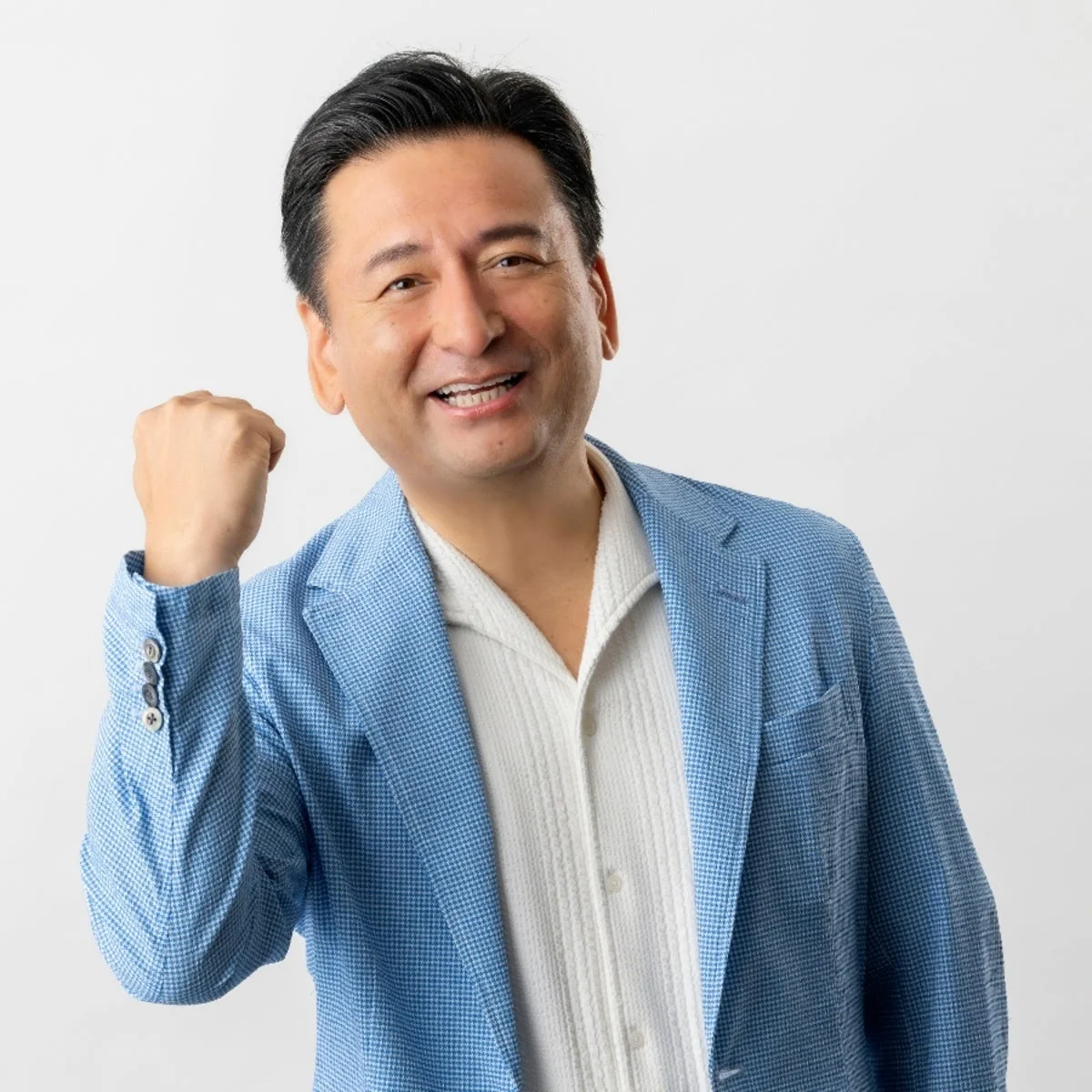 水色のジャケットと白いシャツを着用した男性が、明るい笑顔でガッツポーズをしているポートレートです。自信と喜びにあふれた表情で、前向きな印象を与えます。