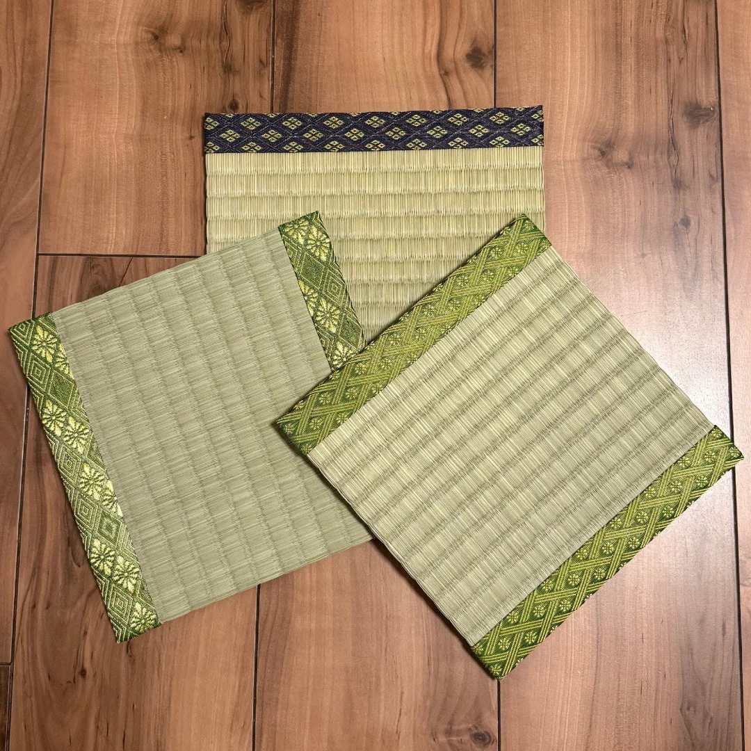 木製の床の上に3枚の小さな畳が置かれています。2枚は緑色の、1枚は濃い青色の縁取りがあり、それぞれ異なる和柄が施されています。