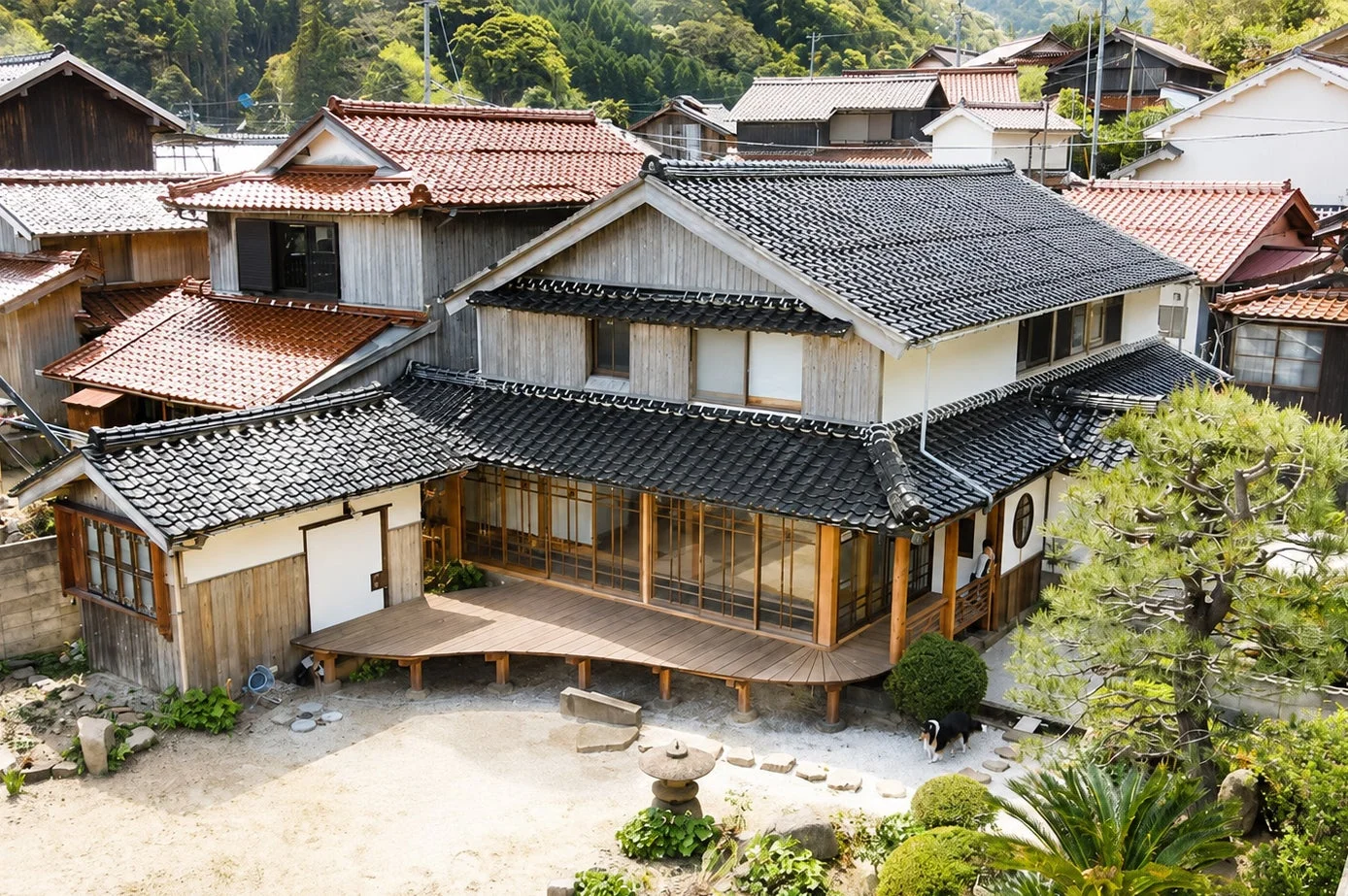 緑豊かな山を背景に、黒と赤の瓦屋根が特徴的な日本の伝統的な家屋が立ち並ぶ集落の風景