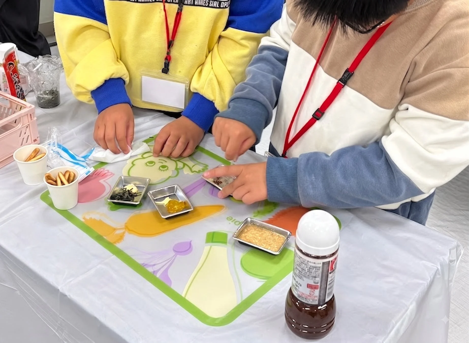 テーブルに並べられた食材の小皿を囲み、2人の子供が調理体験や食育活動に参加している様子。手元に集中し、楽しそうに作業に取り組んでおり、学びの場であることがうかがえる。