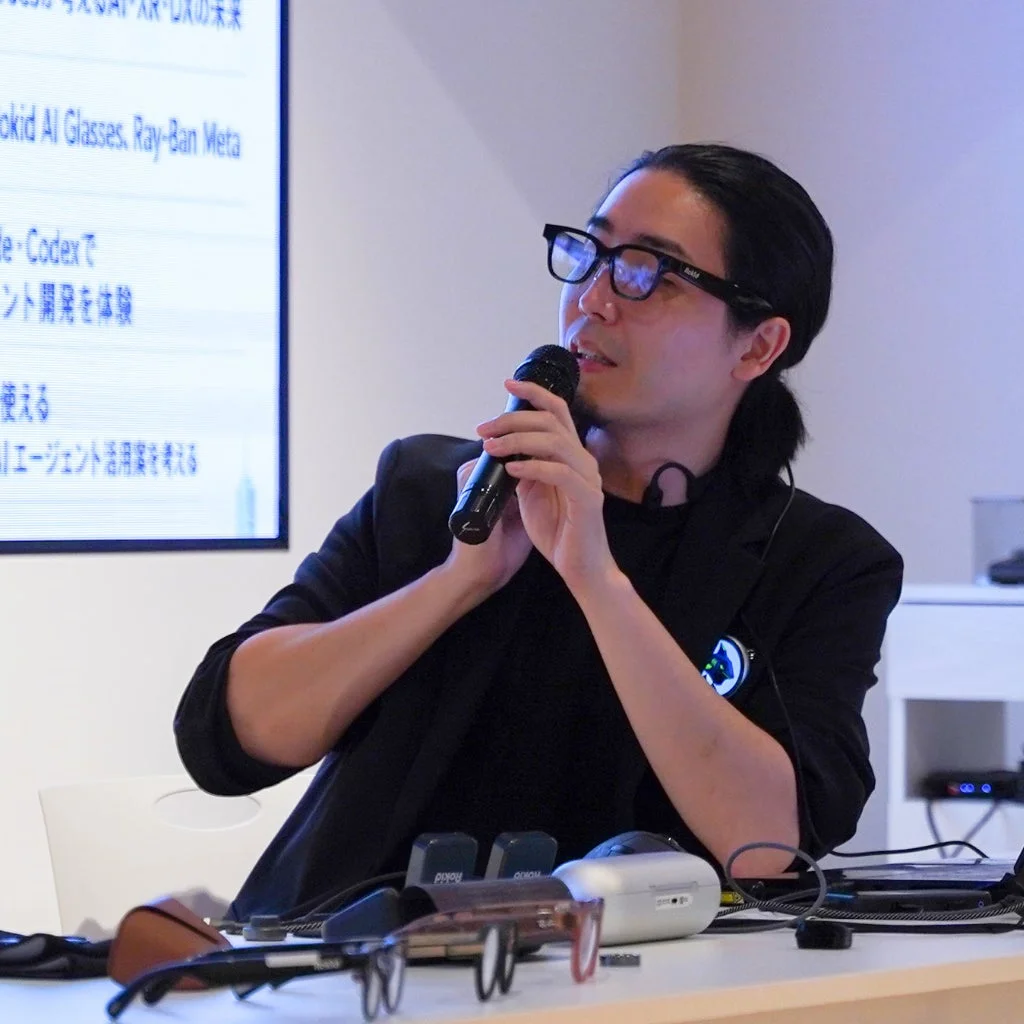 スマートグラスを着用した男性がマイクで講演中。背景にはAIグラスやAIエージェントに関するプレゼン資料