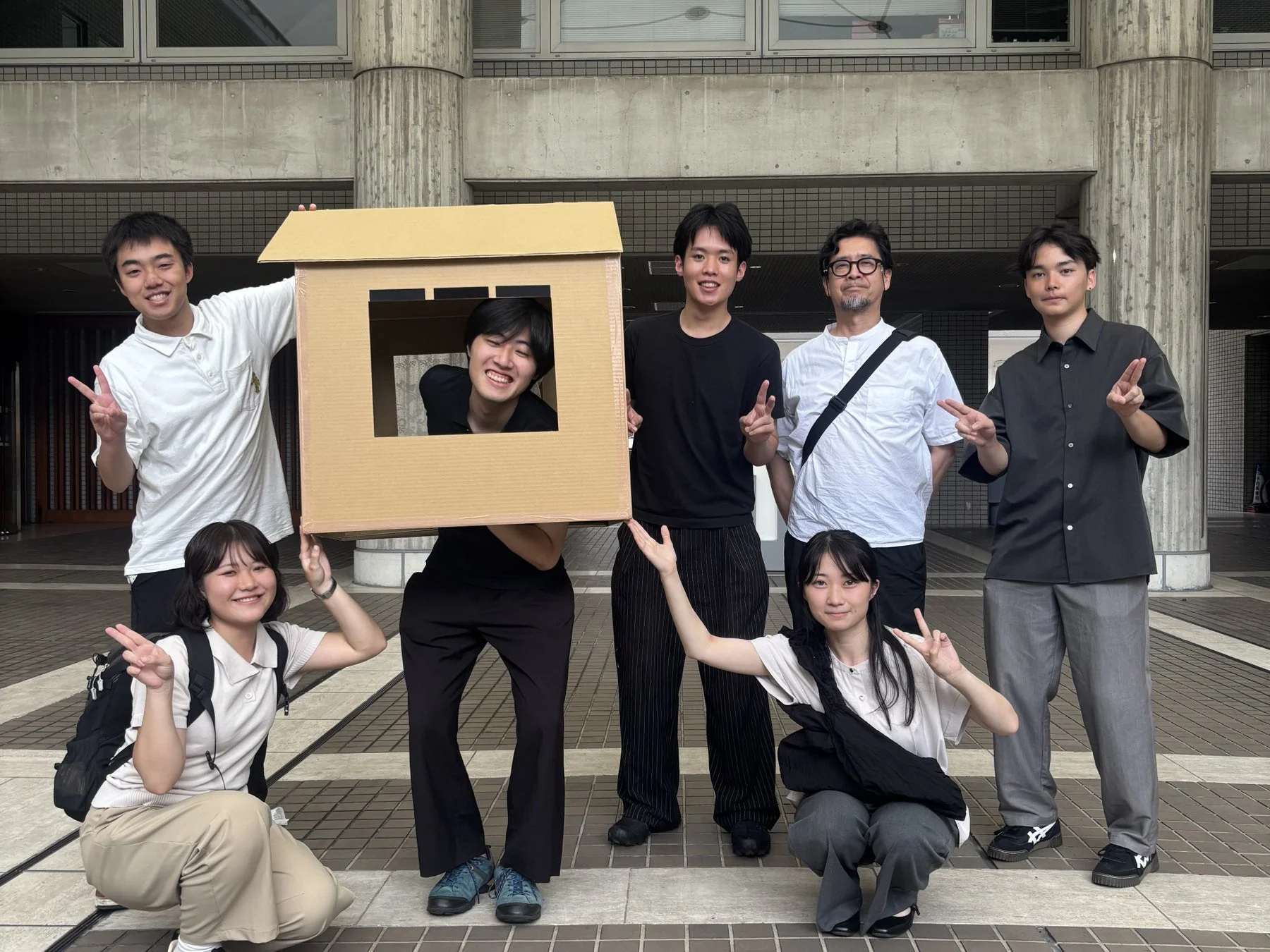 学生たちが段ボールの家を抱えて笑顔でポーズをとっている集合写真