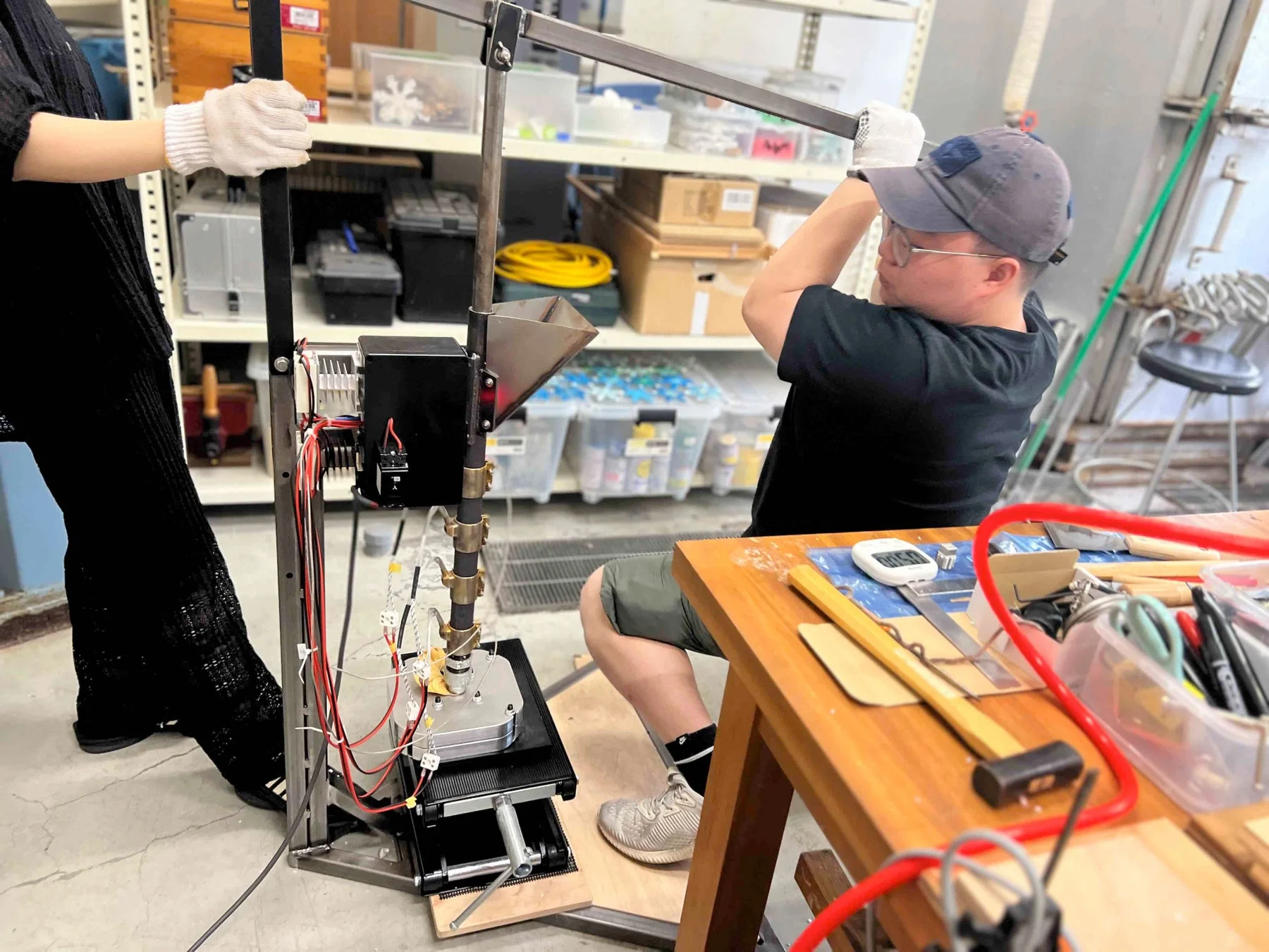 実験室のような空間で、2人の人物が自作と思われる装置を操作している様子